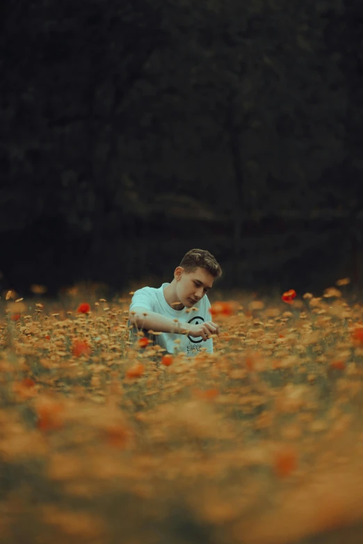 a young man squatting down in a flowery field