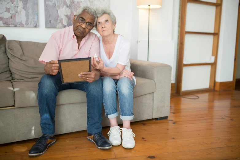 an older couple sitting on a couch, looking at a laptop