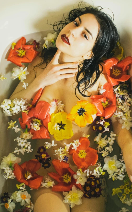 a woman in a bath filled with water with flowers around her