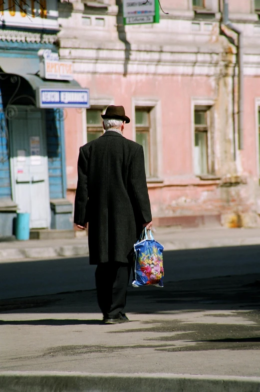 an old man with a shopping bag walks down the street