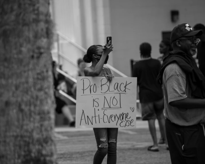 a protester holds a sign as a protestors stand near