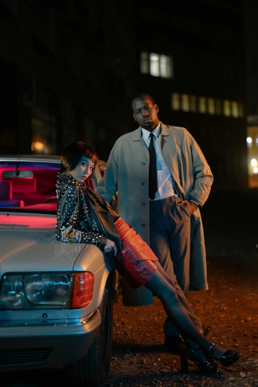 a couple are standing next to their parked car at night