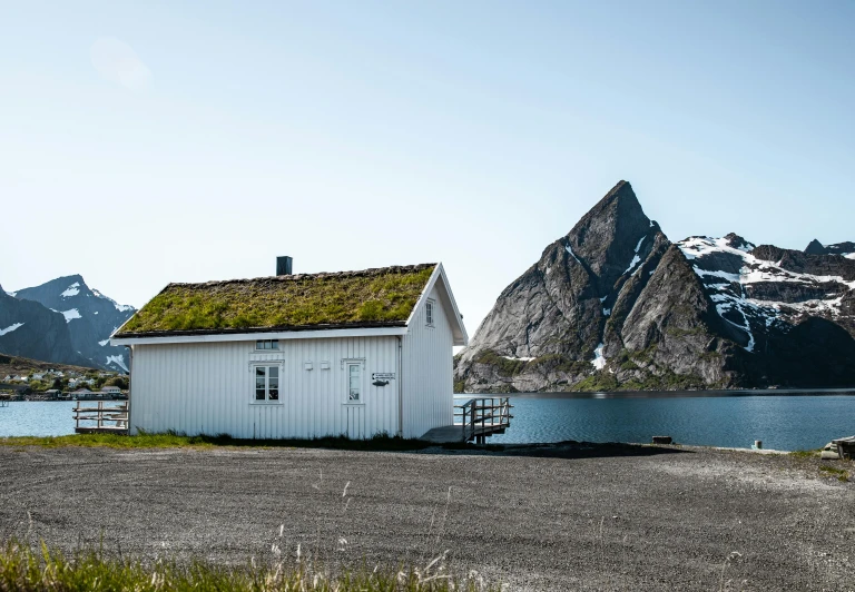 a white cabin next to water and mountains