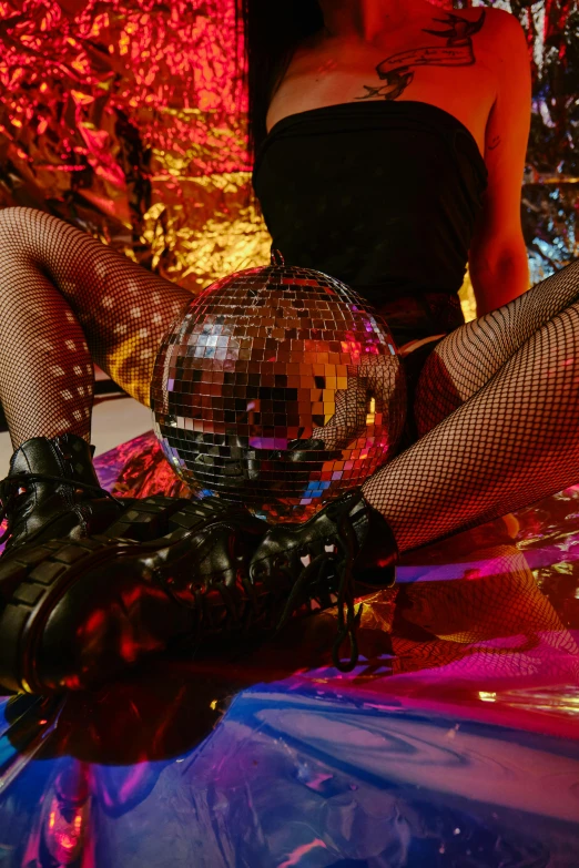 a woman is dressed in fishnet stockings and is sitting on a glass table with a mirror ball