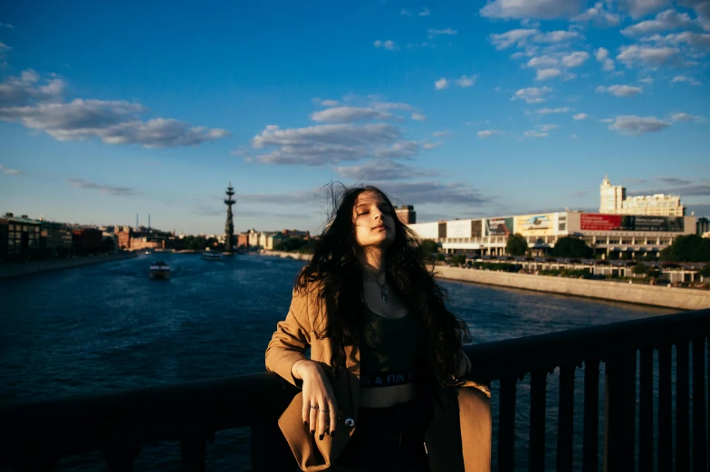 a beautiful young lady with long dark hair leaning against a fence