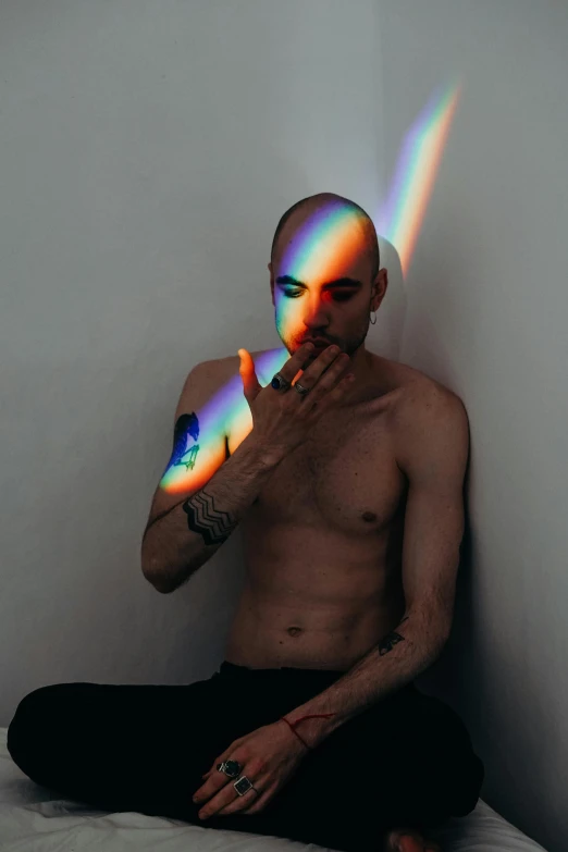 man in black pants sitting on bed in room with rainbow light