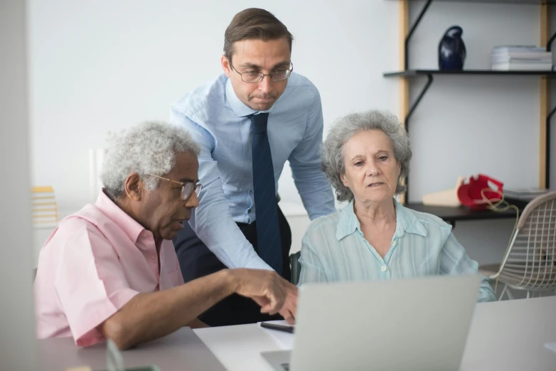 two men looking at an older lady while on a laptop