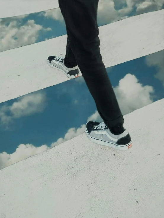 a man standing on a sidewalk reflecting clouds in a mirror pool