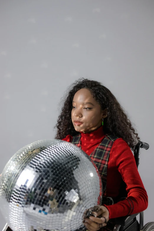 a woman holds onto a mirror ball that is on a wooden bench