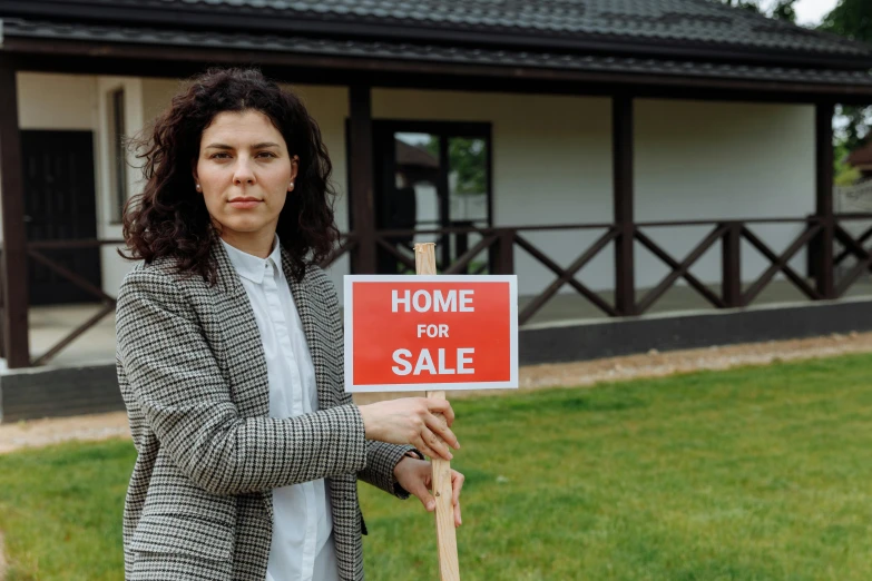 a woman with curly hair standing outside of a house holding a sign