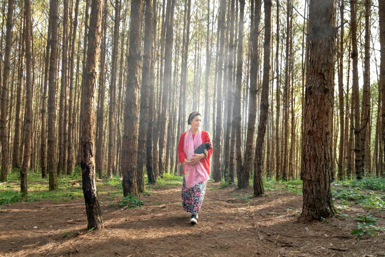 a woman walking through a forest wearing a bright outfit