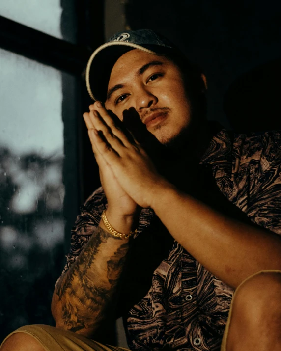 a man wearing a gold celet sits looking out of a window