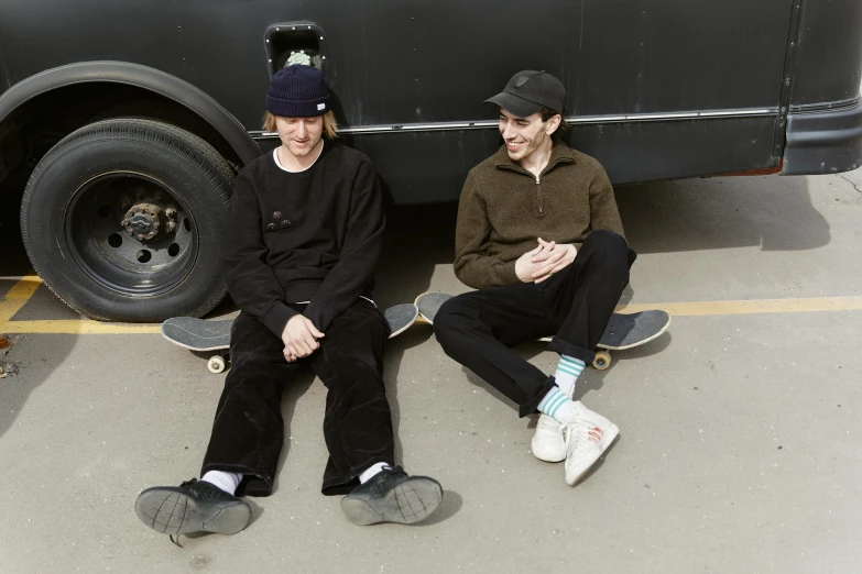 two guys sitting on the pavement near a black van