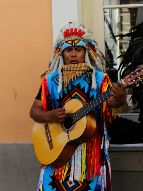 a man in native style clothing plays guitar while holding a large black bird