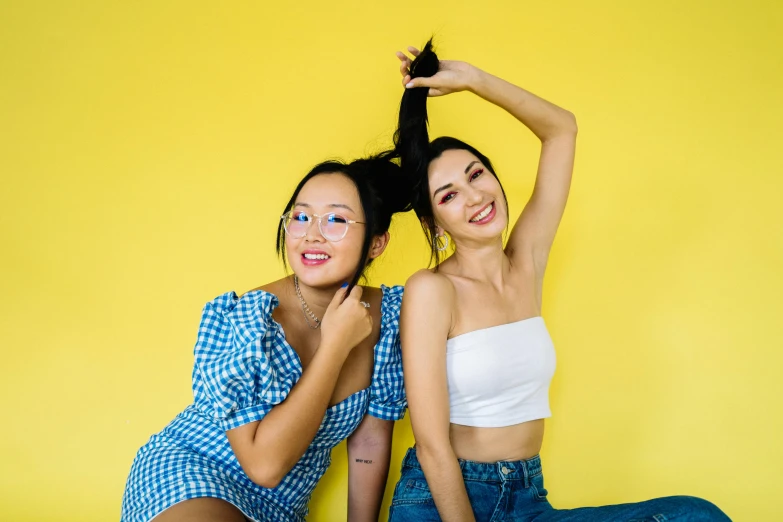 two pretty young ladies sitting on the ground in front of a yellow wall