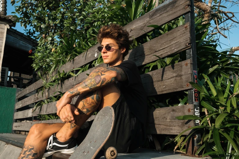 a man with glasses and a tattoo sitting on a skateboard