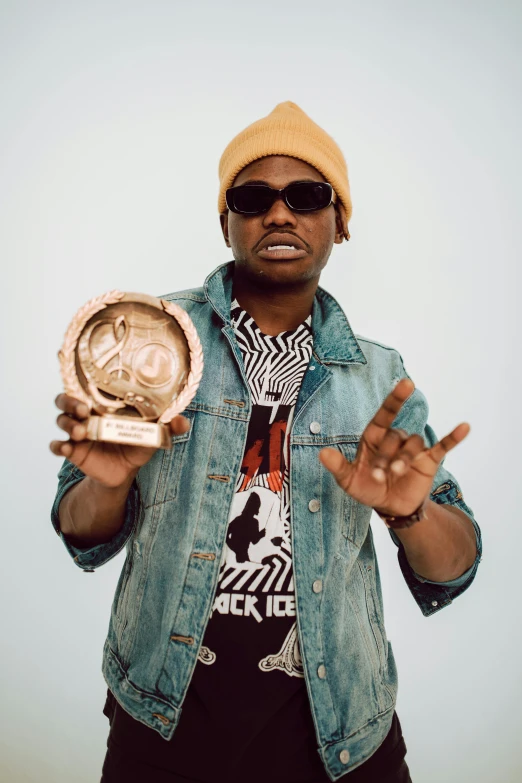 a man with a jean jacket and a hat holds up a peace sign in front of his hands