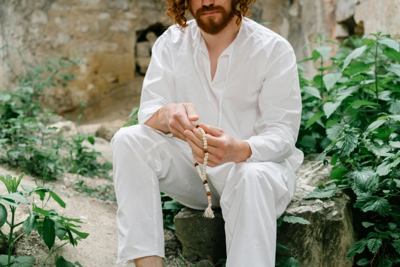 a man in white sitting and wearing some sort of beaded