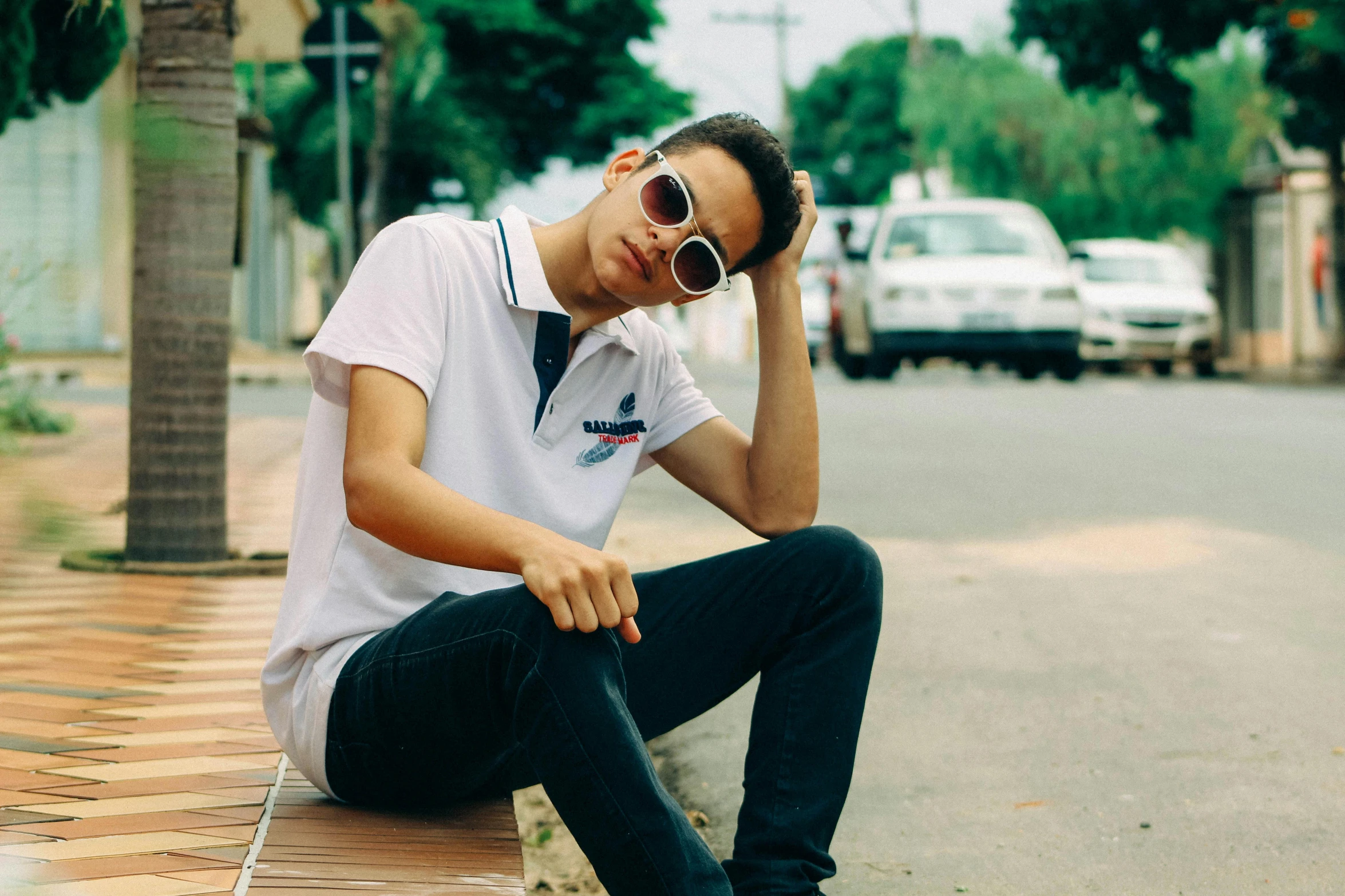 a young man sitting down on a sidewalk