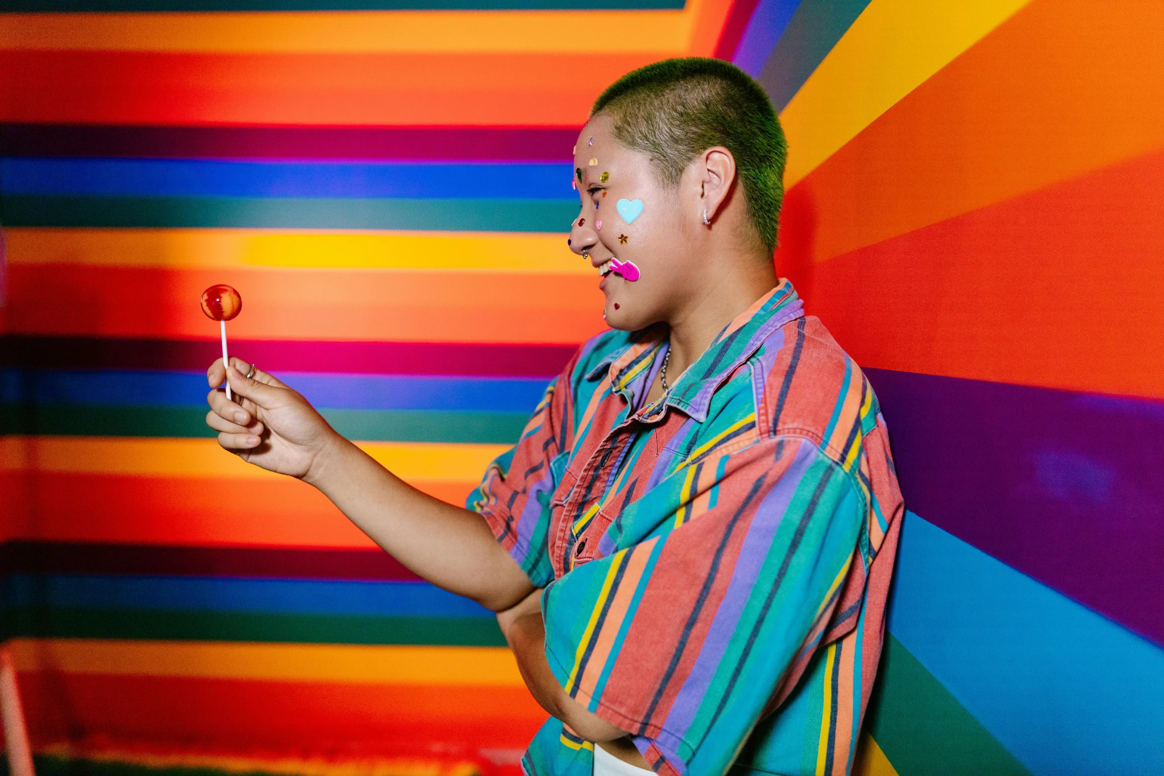 man in front of a colorful striped wall holding a red lollipop