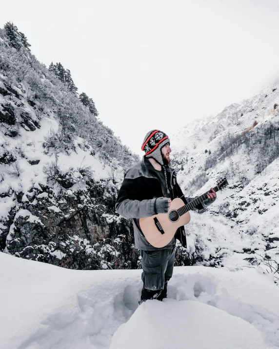 a man holding a guitar standing in a snowy landscape