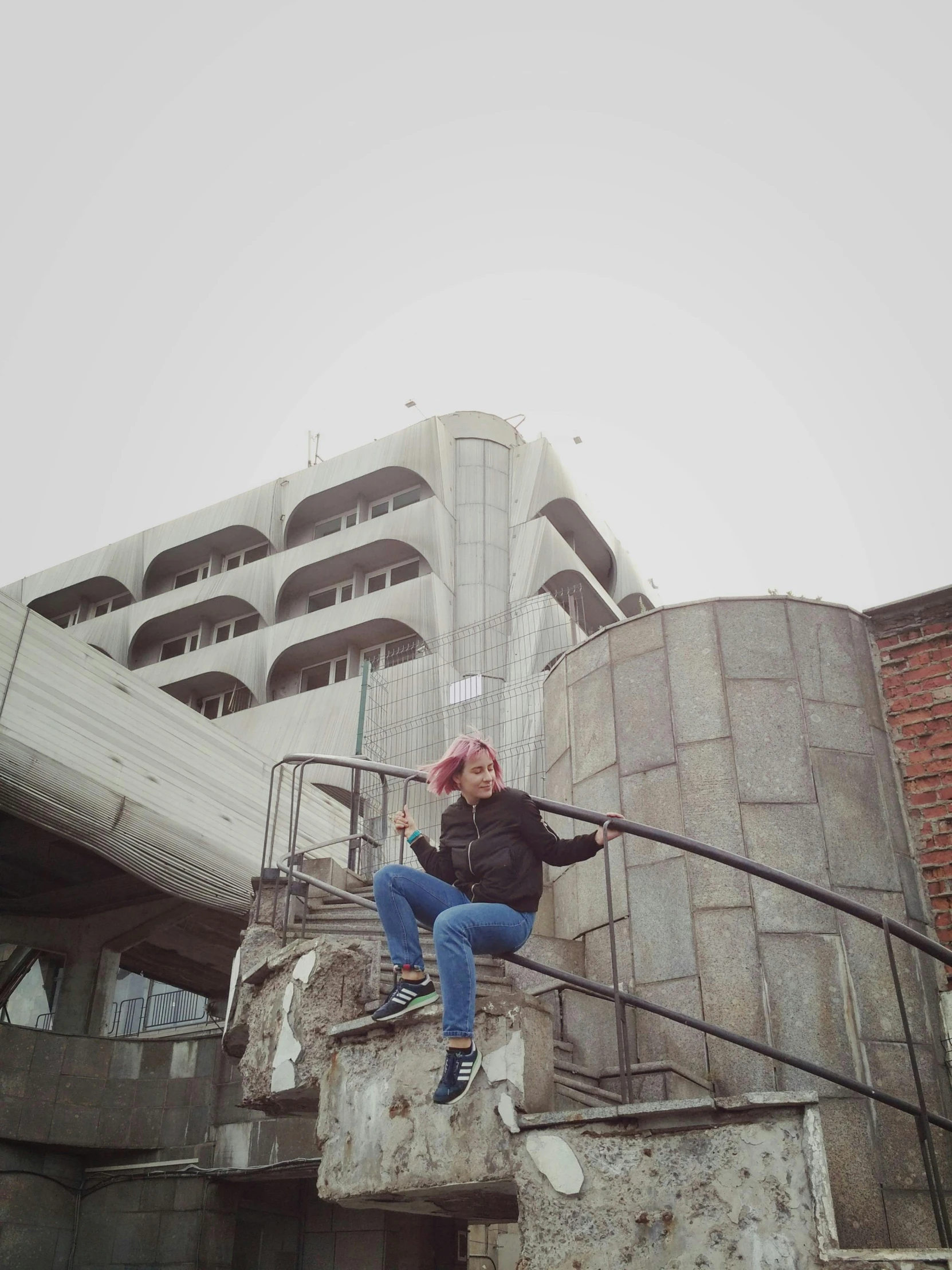 woman in black jacket sitting on stairwell with grey building