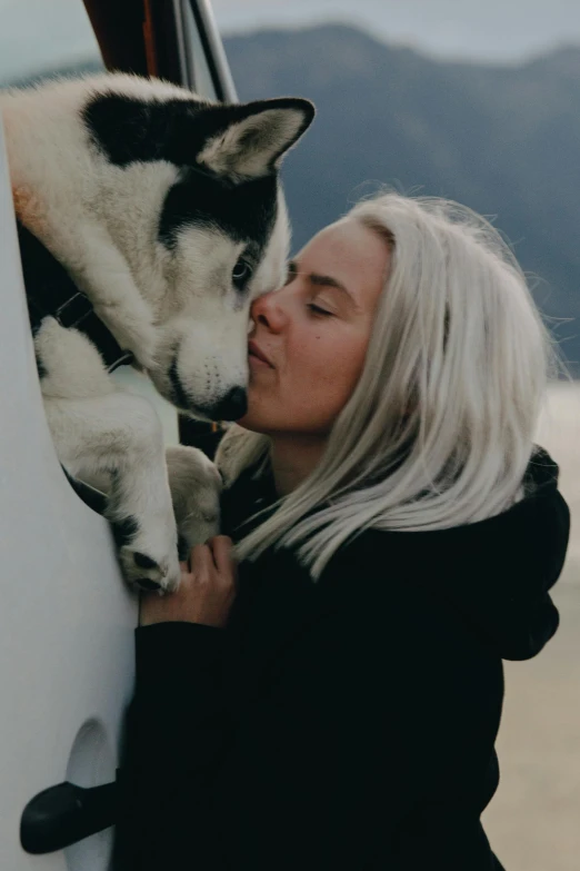 a woman with blonde hair is cuddling up to a husky dog