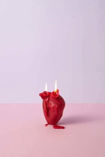a candle is on a pink surface with two burning candles
