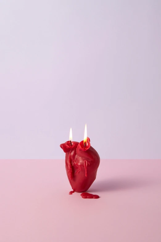 a candle is on a pink surface with two burning candles