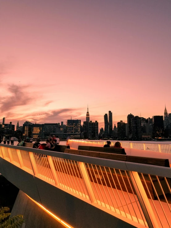 people are on benches on a bridge overlooking the city