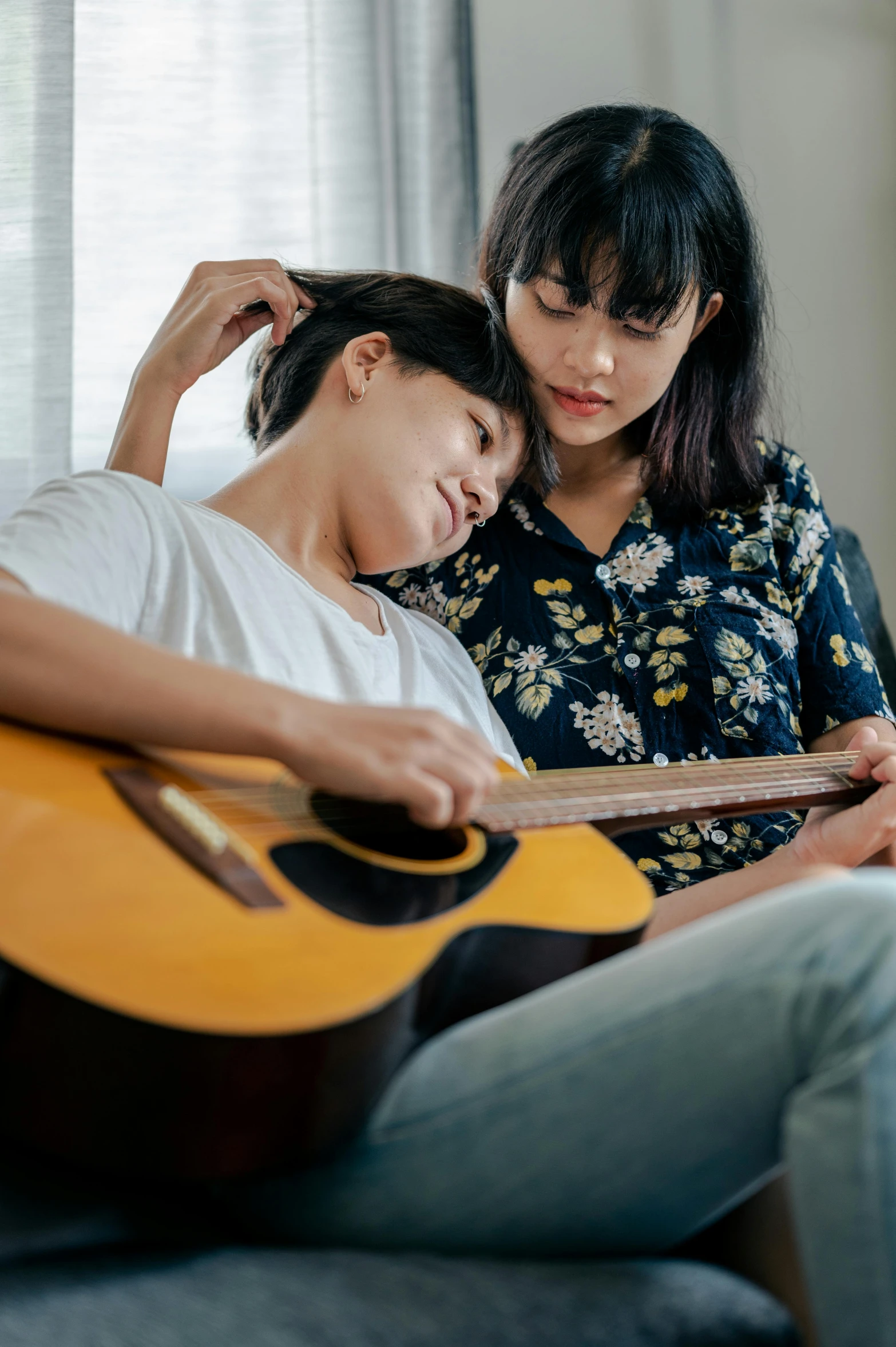 two people sit on the couch and play a guitar