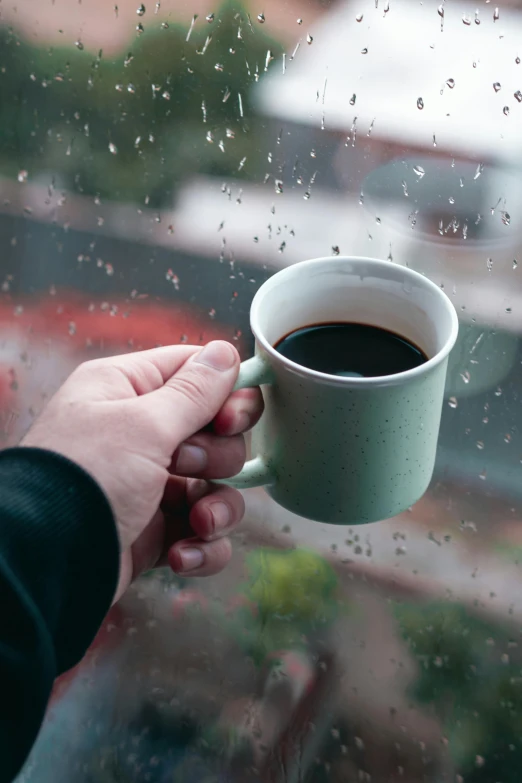 a man holding onto a coffee cup outside the window