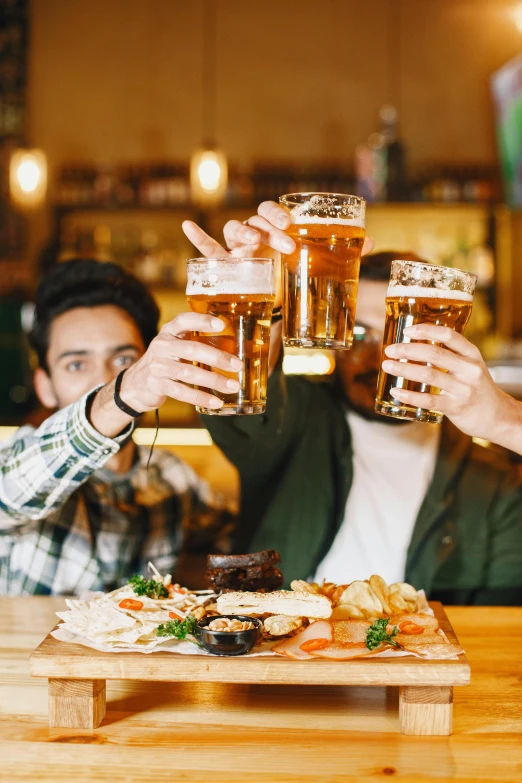 four men toasting with beers while one is holding a platter of food