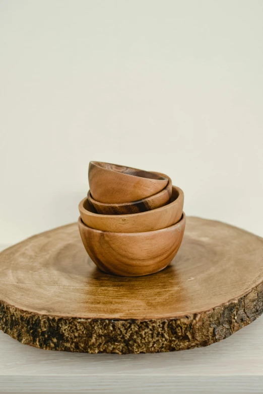 four wooden bowls are stacked on top of a slice of wood