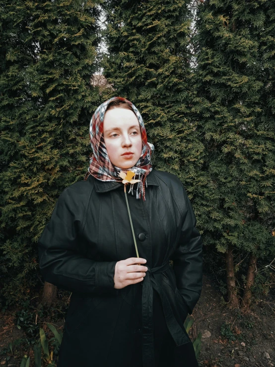 a young woman with a black coat, red plaid bow tie, and yellow flower in her hand