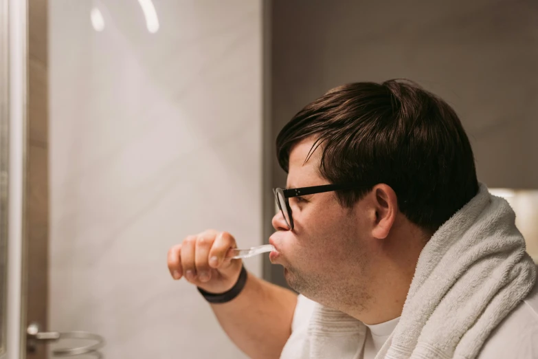 a man wearing glasses brushing his teeth in a bathroom