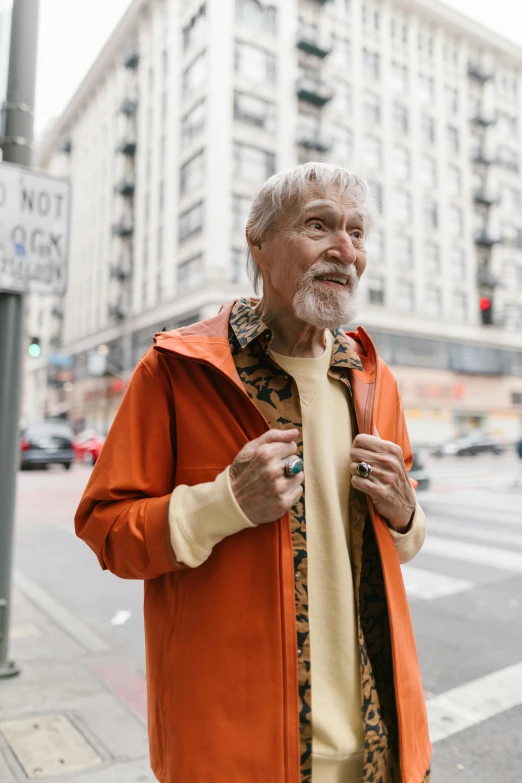 an older man wearing a jacket and leopard print scarf standing on the sidewalk