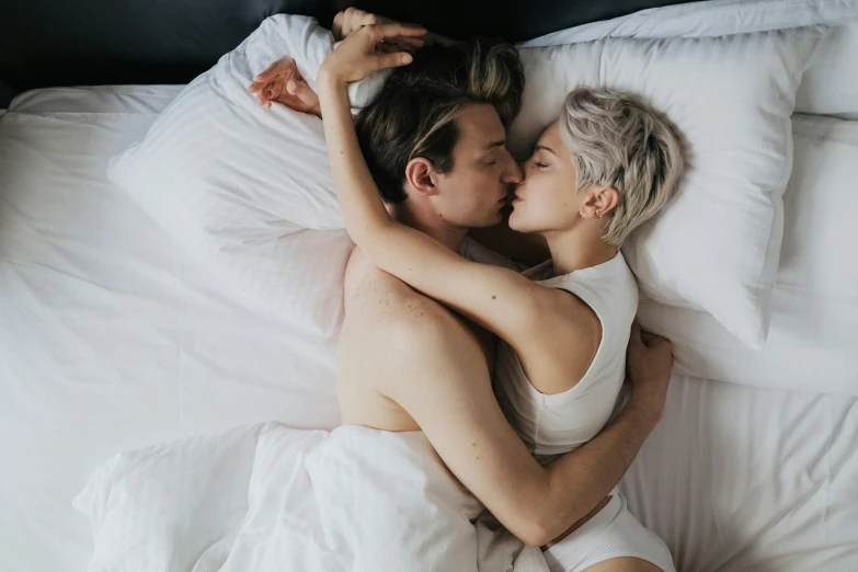 a man and woman cuddle under the covers on a bed