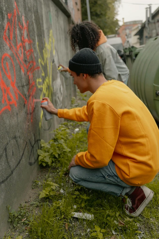 young man writing graffiti on cement wall outside