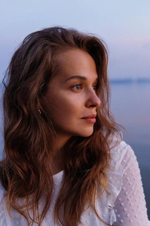 a beautiful woman with long brown hair stands near the sea