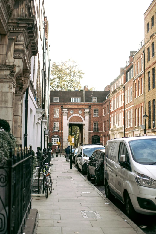 the street is lined with parked cars, and two people walk across