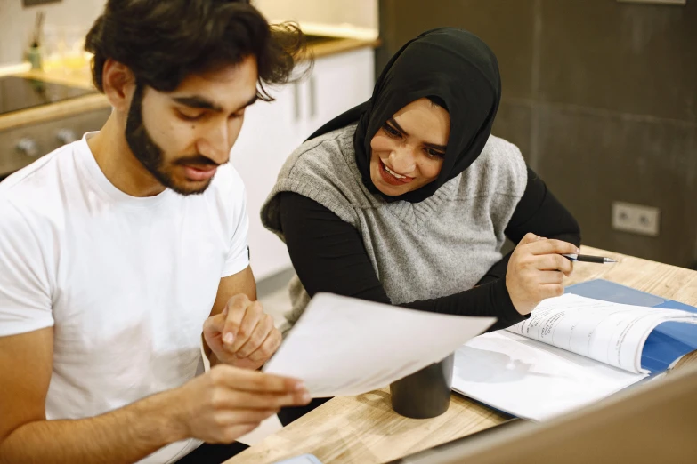an islamic couple are sitting at a table while looking through paperwork