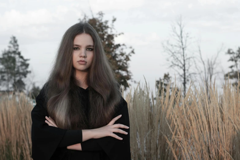 a very long haired woman standing in front of tall grasses