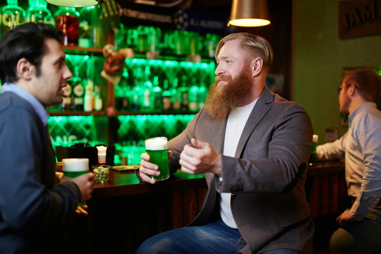 a bearded man drinking a beer with another male bartender at a bar