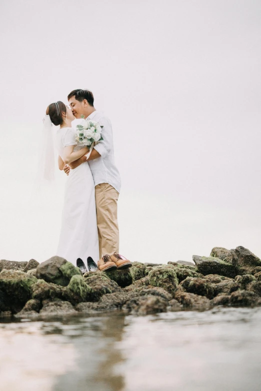 a bride and groom on a rocky shoreline