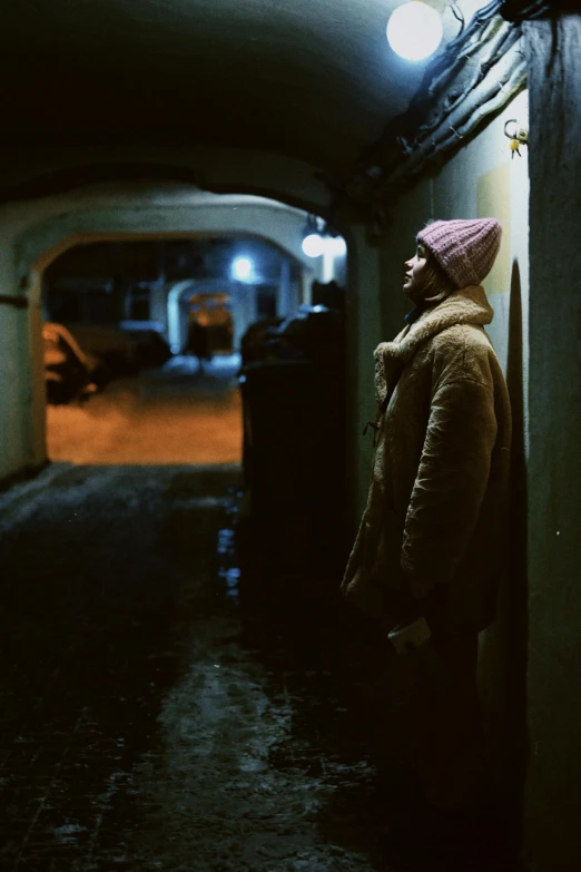 an older woman standing in the dark, wearing a long coat