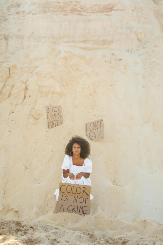 a woman sits in sand with a sign on it