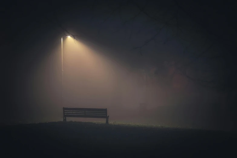 a bench sitting under an empty street light on a foggy night