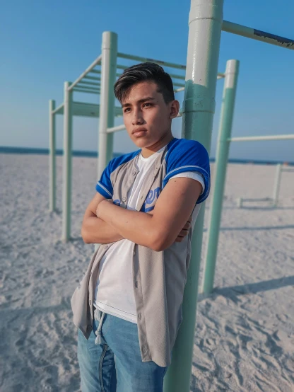 young man leaning on pole by the beach with his arms crossed