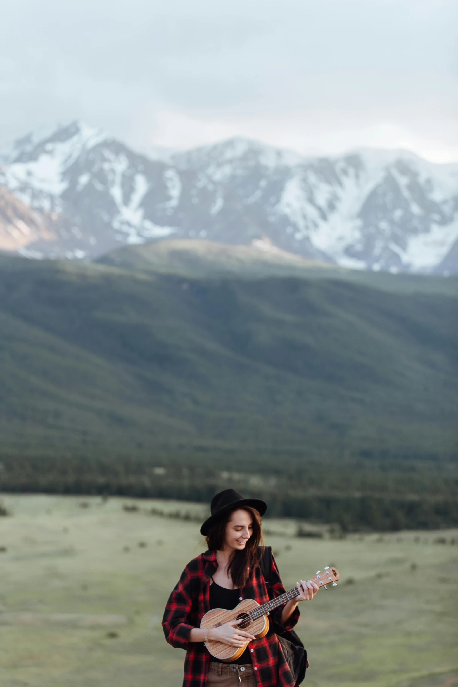 a woman playing a guitar with mountains in the background